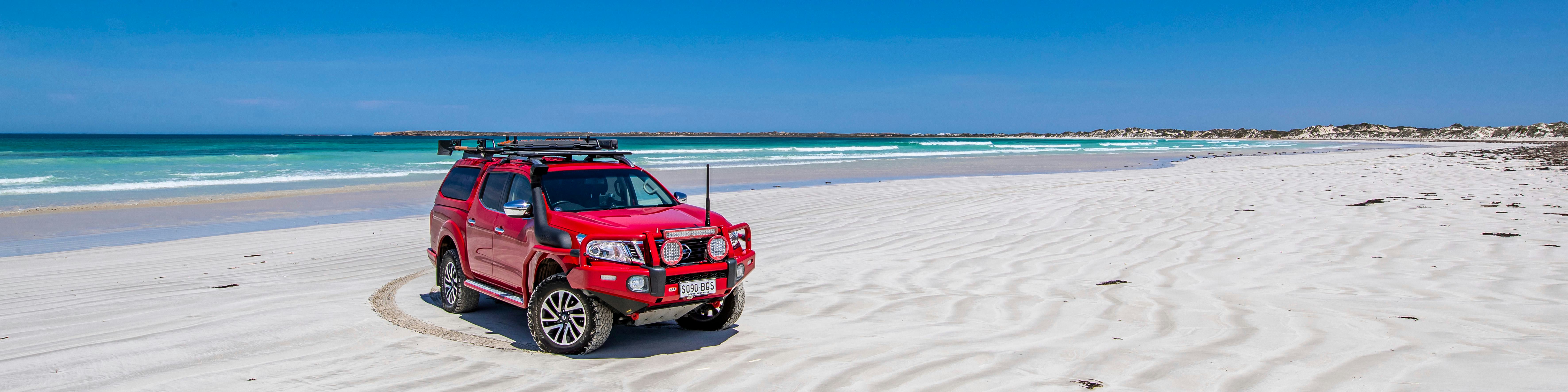 Red 4wd with the latest 4x4 accessories is parked on sandy white beach